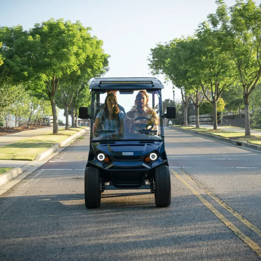 Two people riding a golf cart on a sunny road